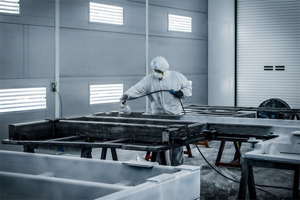 A worker painting large aerospace tooling pieces in a large industrial spray booth