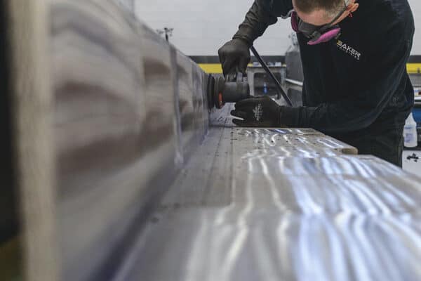 A worker benching a large metal part with a sander