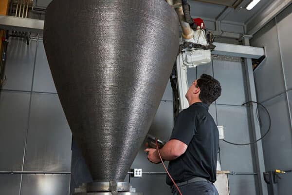 A large metal part and additive manufacturing engineer inside a robotic cell for large-scale 3D metal printing (wire arc additive manufacturing/WAAM)