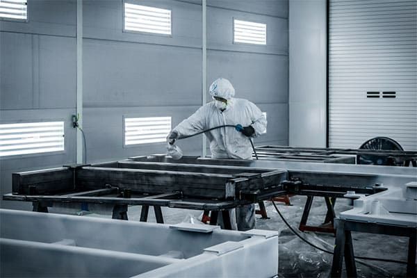 A worker painting large tooling components in an industrial spray booth